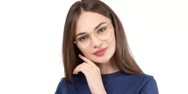 A woman wearing stylish gold-framed eyeglasses and a navy blue shirt, smiling and posing with her hand on her chin.